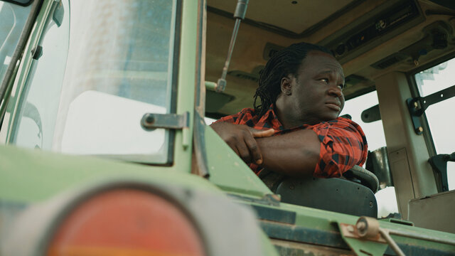 Tired young african farmer sitting in the tractor cabine and looking around. High quality photo