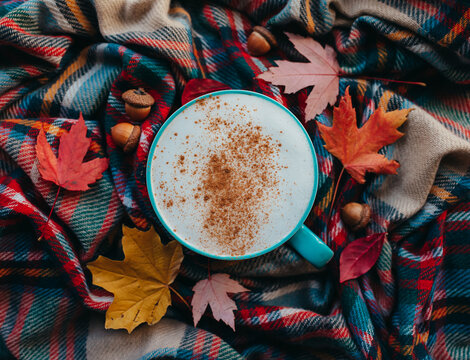 Overhead of pumpkin spice latte on plaid fall scarf with leaves.