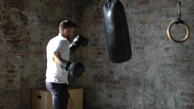 Confident sportsman with muscular body punching boxing bag during training. Young strong man working out for keep fit and healthy. Cross fit training. Motivation, discipline and strength