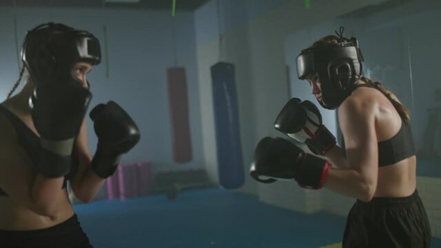 Fight of two female fighters wearing protective helmets, training in the boxing gym, females train defence and series of punches on a battle, 4k slow motion.