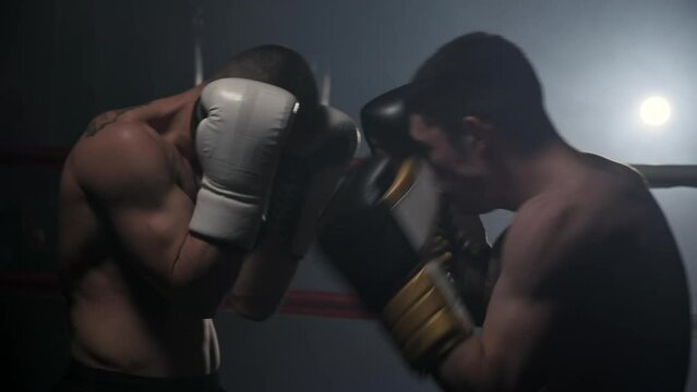 Cinematic slow motion shot of two professional young muscular shirtless male boxers fighting in a boxing ring. High quality FullHD footage