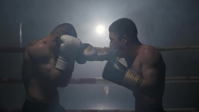 Cinematic slow motion shot of two professional young muscular shirtless male boxers fighting in a boxing ring. High quality FullHD footage