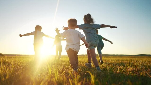 kids run in the park at sunset. friendly family children camp kid dream concept. a group of children run on the grass at the rays fun of the sun silhouette. childhood dream teamwork concept sunset