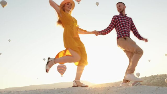 happy young couple at sunrise walking holding hands on the top of the mountain against the background of balloons in Cappadocia, Turkey