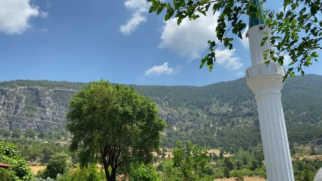 Panoramic view of the mosque on the background of beautiful green mountains, a lonely mosque in the mountains against a blue sky with white clouds closeup concept, trees develop in the wind