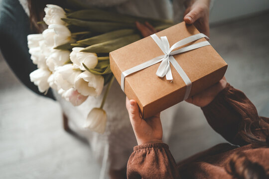 The child's hands hold a beautiful gift box with a ribbon and white tulips. Top view, close-up. Happy mother's day