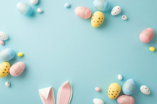 Easter party concept. Top view photo of easter bunny ears white pink blue and yellow eggs on isolated pastel blue background with copyspace in the middle