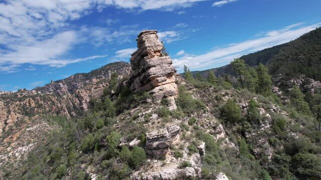 360 degree drone footage of rocky Sedona peak with scattered greenery under blue cloudy sky