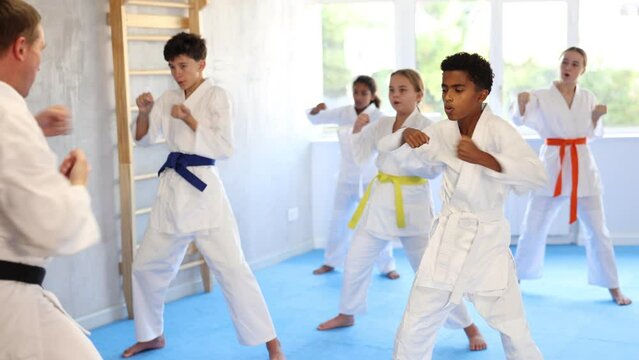 Concentrated black teenager in kimono practicing punches in gym during group martial arts workout. Shadow fight, combat sports training concept. High quality 4k footage