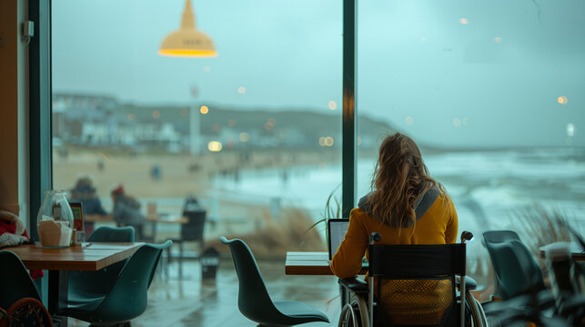 Inclusive image of a happy remote worker with a disability working on laptop in a beach cafe. Positive flexible working company culture. Solopreneur digital nomad working by the sea. 