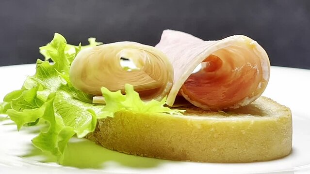 A sandwich with ham and fresh salad rotates on a dark background. Bee-roll with a healthy snack.