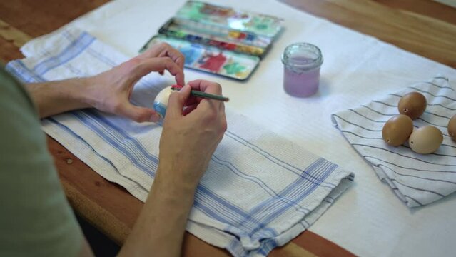 White male painting easter bunny on easter egg with water color