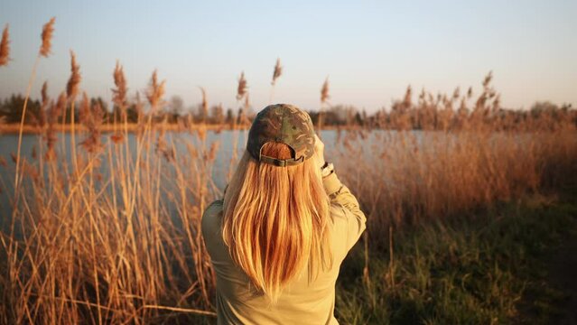 Woman ornithologist with binoculars looking for water birds at lake. Wildlife observation and bird watching. Handheld video