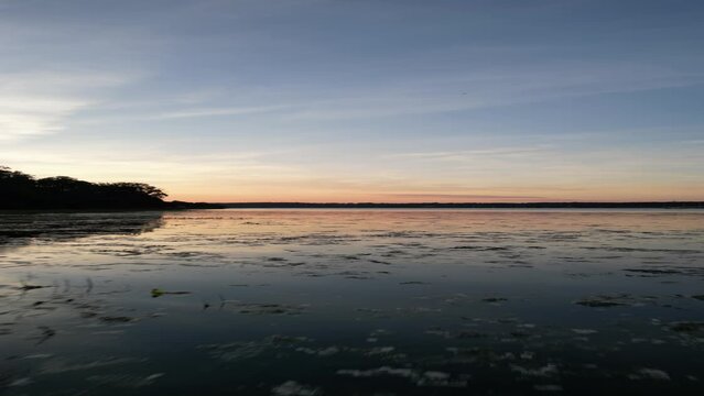 Vertical drone footage of a lake with the reflection of the sunset sky in it