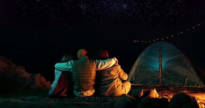 Friends, hug and camping with stars at night for adventure, holiday fun and outdoor activity. Campsite, people and pointing to sky with embrace, tent in nature and travel with hand gesture in woods