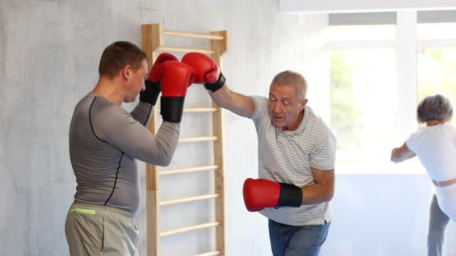 Coach and senior man pupil are engaged during training, boxing classes. Male trainer helps student to work out force of blow, to box quickly and effectively