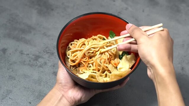 Close-up of a man's hand stirring chicken noodles with seasoning