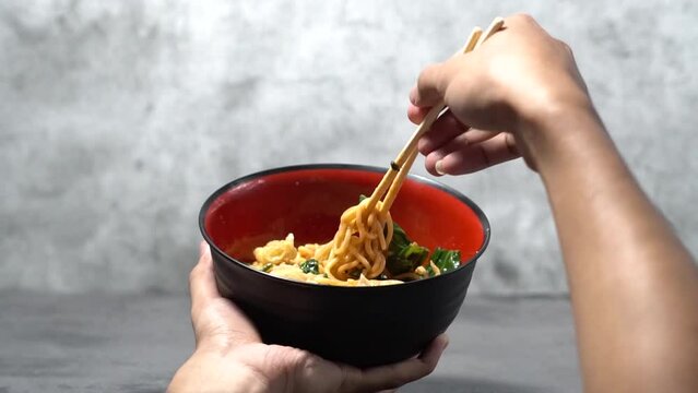 Close-up of a man's hand stirring chicken noodles with seasoning