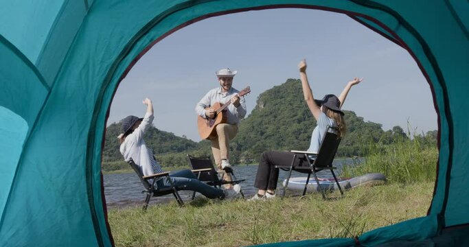 Happy family backpacker playing guitar and singing  while having camping near lake. 4k video