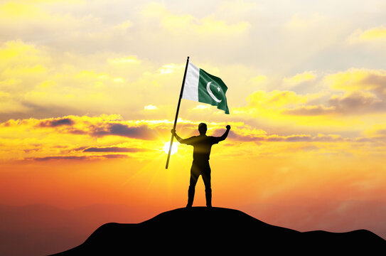 Pakistan flag being waved by a man celebrating success at the top of a mountain against sunset or sunrise. Pakistan flag for Independence Day.