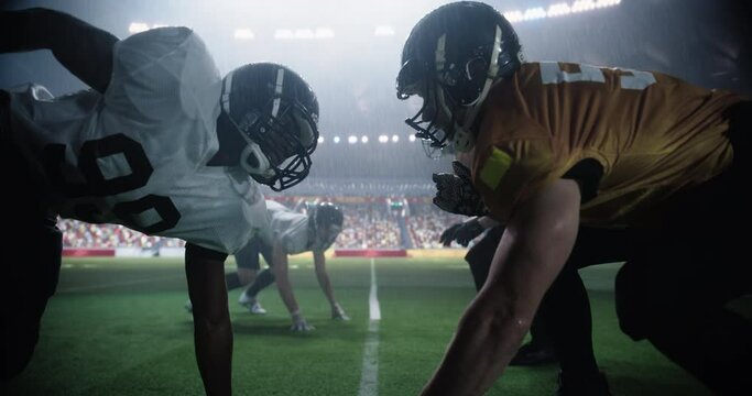 Two Diverse American Football Teams Play a Dynamic Match in Soaking Wet Weather in Front of a Stadium Filled with Spectators. Players Making a Stand-Off Before Quarterback Passes the Ball