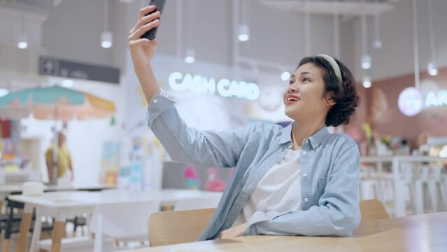 A woman is taking a selfie in a store. The store is brightly lit and has a variety of items for sale. The woman is sitting at a table and she is enjoying her time in the store