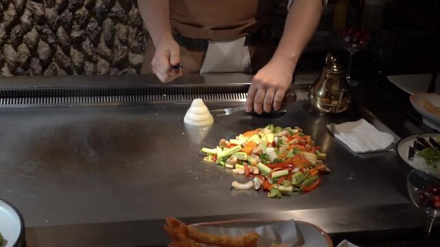 Chef's hand setting fire to a pyramid of chopped onions on a teppanyaki grill