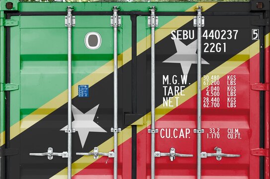 Saint Kitts and Nevis flag depicted on metal doors of shipping cargo container outdoors in docks area close up