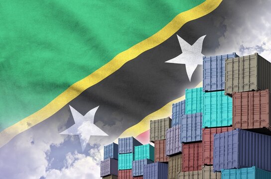 Saint Kitts and Nevis flag and big stack of shipping cargo containers in docks with sky background close up