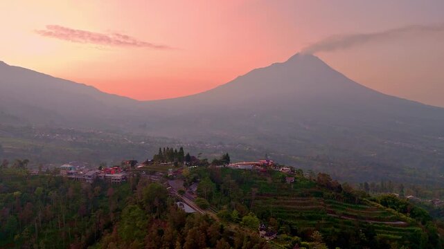 Aerial view of hill with tourist destination building with beautiful sunrise sky and mountain on the background. Ketep Pass Tourist destination with view of Mount Merbabu and Merapi Volcano. 4K drone