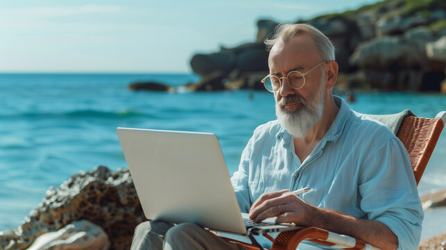 The image depicts a man working remotely as a digital nomad by the beach. He is seated at an outdoor table with his laptop, fully engaged in his work