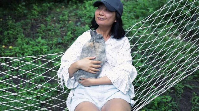 Asian girl lies on hammock in summer garden with Easter bunny. 