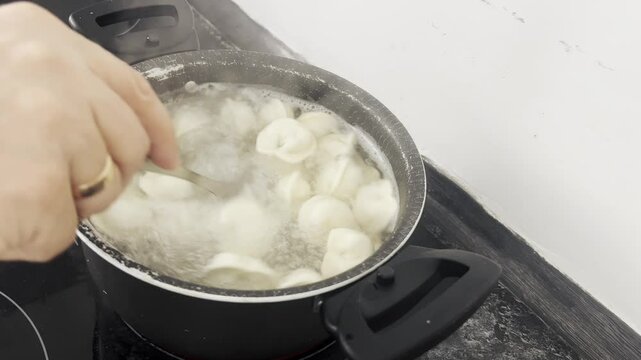 Dumplings boiling in water are stirred with a large spoon when cooking.