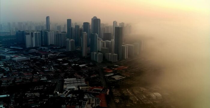 morning aerial drone footage of a city with high-rise buildings and business skyscrapers covered in fog and clouds, pollution