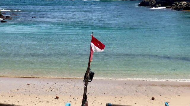 closeup indonesia flag flies on wooden pole isolated in sandy beach and ocean.