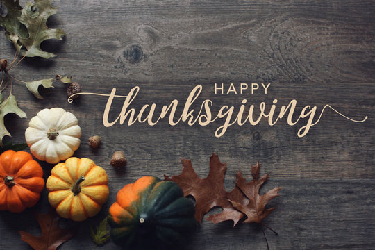 Happy Thanksgiving greeting text with colorful pumpkins, squash and leaves over dark wooden background