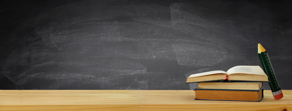 back to school banner. stack of books over wooden desk in front of blackboard.