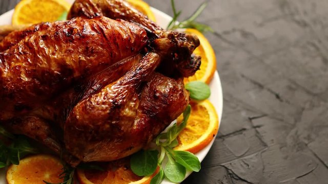 Roasted whole chicken or turkey served in white ceramic plate with oranges and lamb's lettuce on dark stone background. View from above.