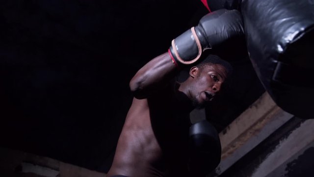 Sportsman training his fist hitting boxing bag low angle close up shot in smoke