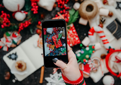 Woman's hand take a mobile photo of christmas composition. Smartphone with mobile camera display while shooting. Top view