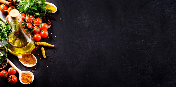 Food background. Top view of olive oil, cherry tomato, herbs and spices on rustic black slate. Colorful food ingredients border.