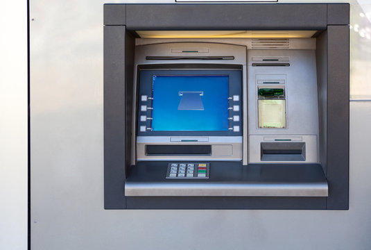 Silver atm machine with screen and buttons is in building wall, nobody