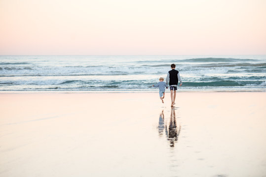 Teen boy holding little brother's hand on beach