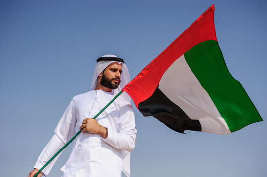 Proud arabian Emirati man holding a UAE flag in the desert.