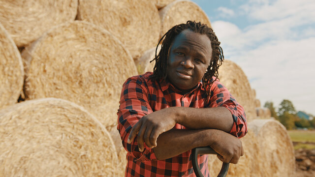 Young african farmer resting on the pitchfork handle. Hay roll stack in the background. High quality photo