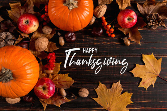 Thanksgiving greetings. Dry yellow leaves, pumpkins, berries, nuts and frame on a wooden background, top view. Kaligraphic capital inscription.