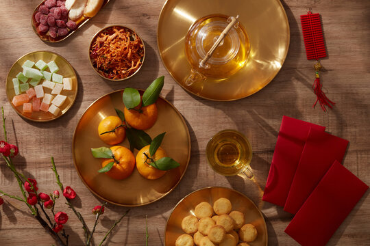 Tet holiday with mandarin orange teapot in golden dish candy jam , fried potato flower red pocket biscuit  in wooden background , photography Tet holiday content , chinese new year