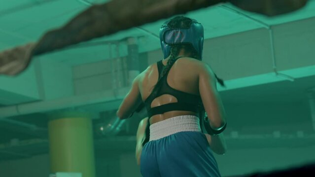 Two female boxers in helmets and boxing gloves fighting in ring at gym. Young sportswoman hitting sparring partner, knocking her out. Sport, boxing concept