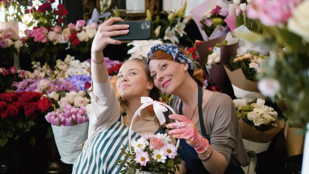 Beautiful teenager girl takes a selfie photo with her mother in a personal flower shop. Florist workers with aprons in a flower shop posing for selfie photos for social networks