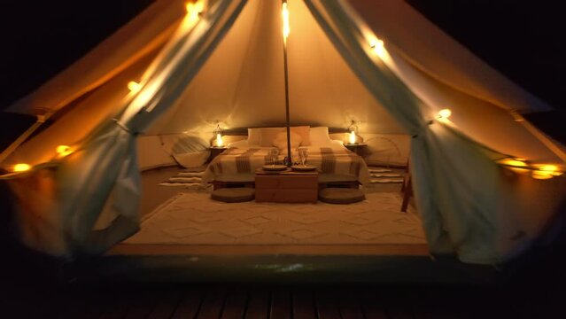 Drone view of tent exterior and interior with bed and illumination at glamping, forest around, night